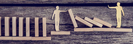 Wide panorama view of silhouette cutout of a man holding up fallen dominos as other person pushes them down, toned retro effect.の写真素材