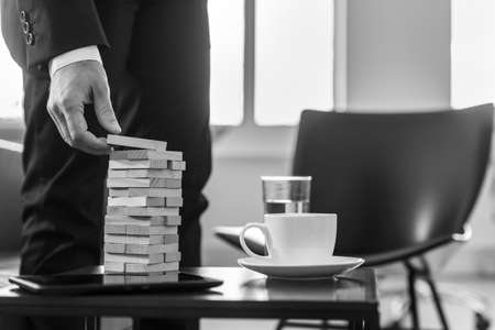 Monochrome image of a business man in an office building a tower of wood blocks, strategy concept.の写真素材