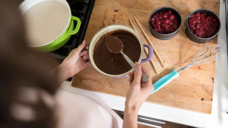 Woman making chocolate desert with raspberries in her kitchen viewed over the shoulder from above.