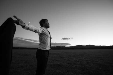 Monochrome image of successful business man in elegant white shirt and tie with his arms outspread standing outdoors in nature.の写真素材