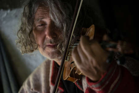 Elderly man immersed in his music as he plays a violin in a close up cropped view of his face.の写真素材