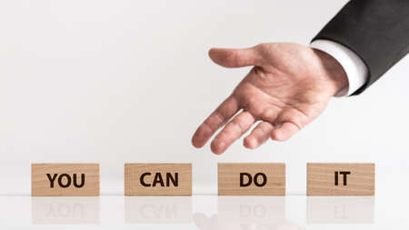You can do it business concept with copy space. Businessman hand showing wooden blocks with inscription, viewed in close-up against light background.の写真素材