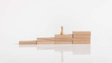 Pawn chess piece on a steps of wooden pegs on a reflective white surface.の写真素材
