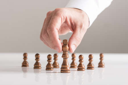 Man playing a game of chess on white table in a close up view of his hand moving a piece conceptual...