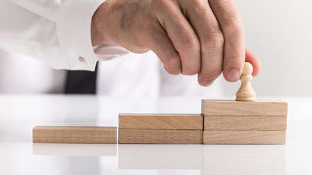 Businessman placing a chess piece on wooden blocks arranged as steps in a concept of success,...