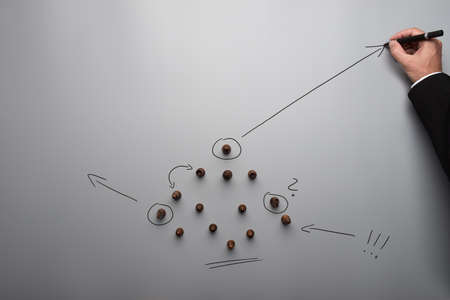 Top view of chess figures placed on grey table with hand of a businessman drawing strategic moves...