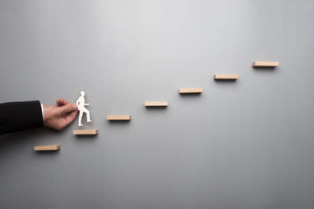 Businessman in white shirt building a graph or ladder of success on grey background.