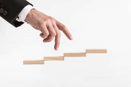 Businessman walking his fingers up steps formed by wooden blocks over white background.の写真素材