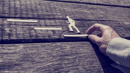 Retro toned image of businessman supporting paper cut out of a man climbing the steps over rustic wood background.の写真素材