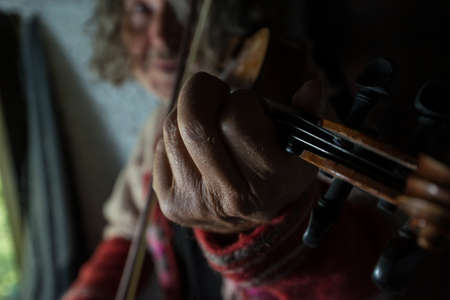 Man playing music on violin indoors with focus to his hand.