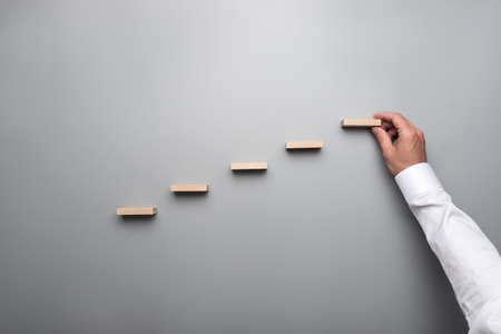 Businessman in white shirt building a graph or ladder of success on grey background.