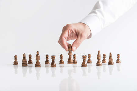 Businessman playing chess moving dark king piece lifting it up in his fingers on white table.