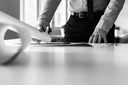 Monochrome image of businessman working on blueprints in an office in a low angle view across the table with foreground copyspace.の写真素材