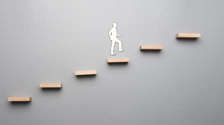 Cut outs of paper man climbing the steps to success in a conceptual image over gray background.の写真素材