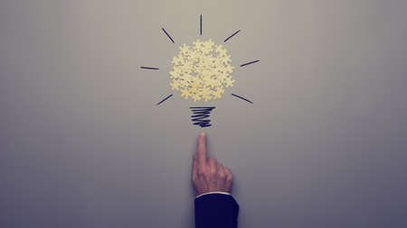 Retro toned image of a businessman pointing on a light bulb drawing with yellow puzzle pieces over grey background.の写真素材