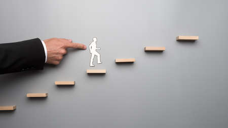 Man using his finger pushing paper human figure climbing steps over gray background.の写真素材