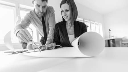 Two co-workers sketching architectural project on large sheet of paper using compass.