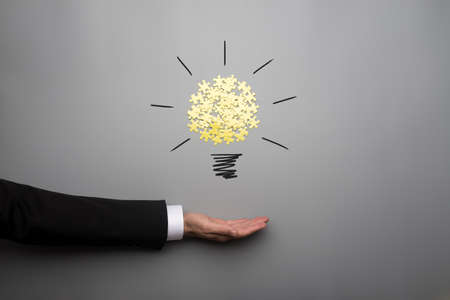 Conceptual bulb drawing with yellow scattered puzzle pieces over open businessman hand on gray background.の写真素材