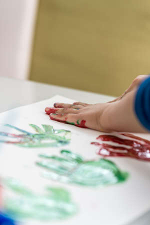 Child having fun with finger paints creating colourful palm prints on a sheet of white paper.の写真素材