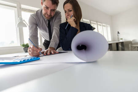 Two architects at work in their office with the man drawing using a set square and thoughtful woman...