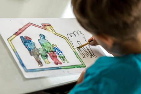 Child colouring in a sketch of a family using a paintbrush and watercolour paints.の写真素材