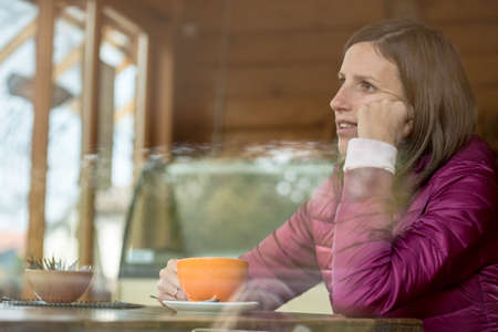 Profile view of a young woman sitting in a bar alone drinking coffee and leaning her head on her...