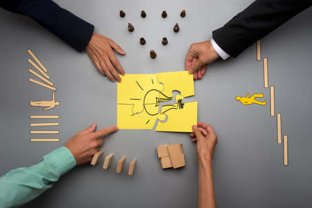 Top view of four business people assembling yellow light bulb with puzzle pieces with various...