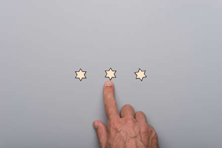 Male hand pointing at on of three paper cut stars placed in a line over grey background.の写真素材