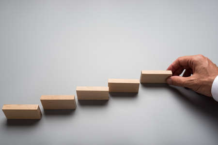 Businessman placing wooden pegs or dominos on grey surface. Conceptual of business vision and start up.の写真素材