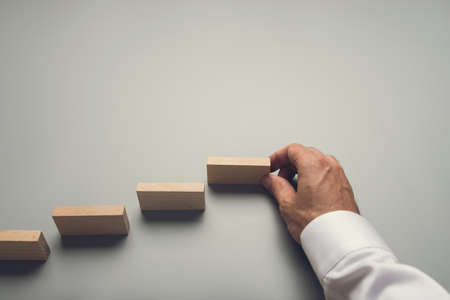 Businessman making steps towards success by placing wooden pegs on grey background.の写真素材