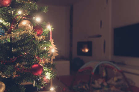 Retro image of decorated Christmas tree with lights indoors in living room with fire place and baby playground.の写真素材