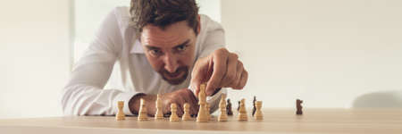 Business executive leaning toward his office desk to precisely place chess figures across the desk with king as the leader.の写真素材