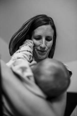 Monochrome image of young mother lovingly holding her baby and playing with her little hand.の写真素材