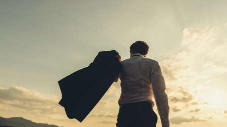 Retro image of successful young businessman standing under glorious evening sky confidently swishing his jacket over his shoulder.の写真素材