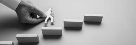 Black and white wide view image of a businessman holding paper cut man climbing up the stairs of wooden pegs.の写真素材