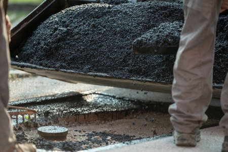 Construction workers applying gravel and cement to a bump in the road to make new asphalt pavement.の写真素材
