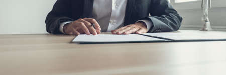 Wide view image of businessman sitting at his office desk with pen in one hand reading a document in...