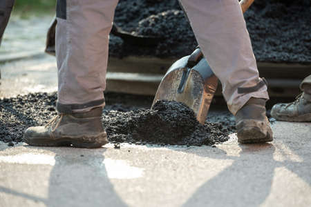 Closeup low angle view of worker arranging fresh asphalt mixture with shovel to patch a bump in the...