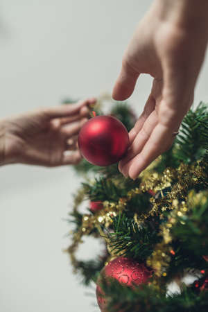 Low angle view of female hand placing red holiday ball on Christmas tree. With retro filter effect.
