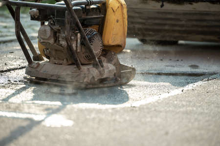 Compactor finishing the last phase of laying new asphalt to patch a bump in the road.