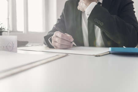 Financial advisor working on document with receipts, paperwork and calculator on his office desk.