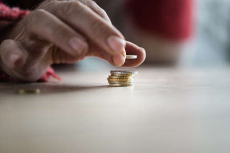Closeup of male senior hands stacking Euro coins. Conceptual of poverty and personal crisis.の写真素材