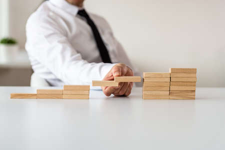 Business leader making plans for the future in a conceptual image as he supports two of the steps made of wooden pegs.の写真素材
