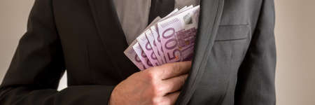 Wide view image of businessman placing five hundred Euro bills in the inner pocket of his suit...