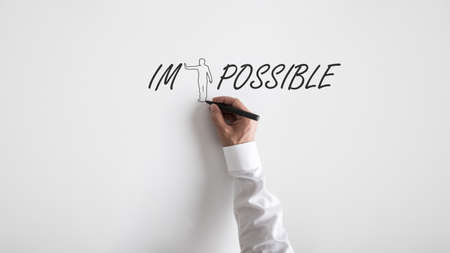 Male hand drawing a shape of a person to push away letters IM from the word impossible over white...