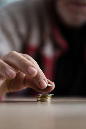 Closeup of senior homeless man counting coins on wooden desk stacking them.
