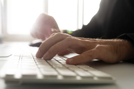 Closeup view of computer programmer working using white keyboard with bright sun light from office windows in the background.の写真素材