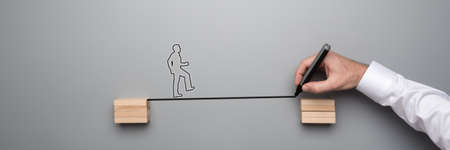 Businessman drawing a black line between two wooden blocks over grey background with silhouette of an entrepreneur walking across.の写真素材