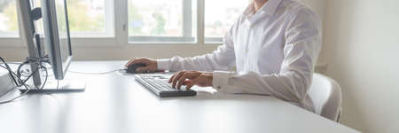 Wide view image of a student or programmer sitting at his desk working on office computer using keypad and mouse.の写真素材