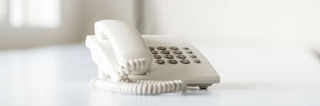 Wide view image of white landline telephone on white office desk.
